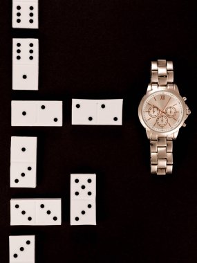 top view of luxury wristwatch lying near dominoes isolated on black clipart