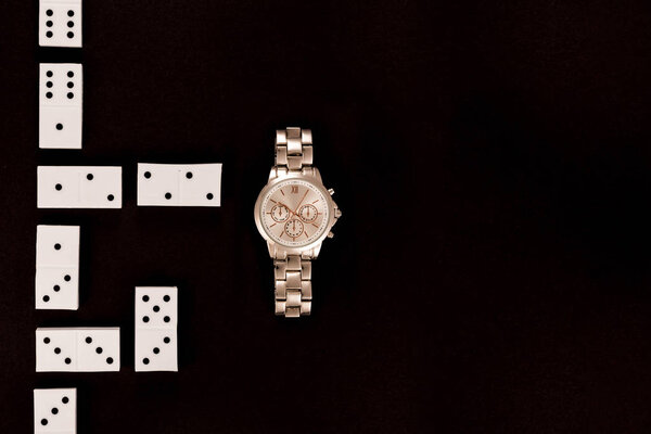 top view of luxury wristwatch lying near dominoes isolated on black