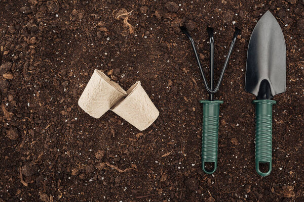 верхний вид использованных бумажных стаканчиков рядом с грабли и лопаты на земле, защищая концепцию природы
 