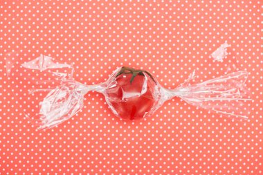 top view of red fresh tomato in transparent candy shaped wrapping on red dotted background clipart