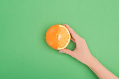 cropped view of female hand with fresh partially cut orange on green background clipart