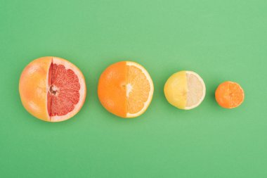 top view of fresh partially cut grapefruit, orange, lemon and tangerine on green background clipart