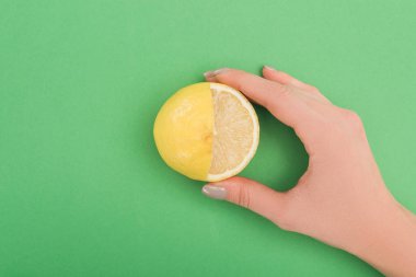 partial view of woman holding fresh partially cut lemon on green background clipart