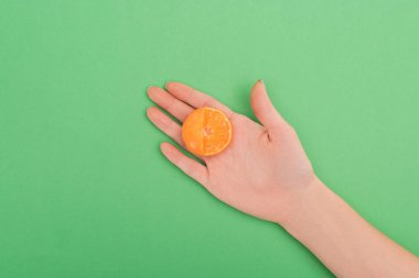 partial view of female hand with partially cut tangerine on green background clipart