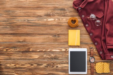 Ahşap arka plan üzerinde gömlek, dijital tablet ve casual aksesuar üstten görünüm