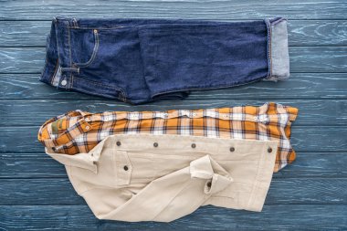 Ahşap arka plan üzerinde kot pantolon, kareli gömlek ve ceket üstten görünüm