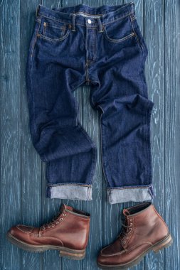 Top view of jeans and brown leather boots on wooden background clipart