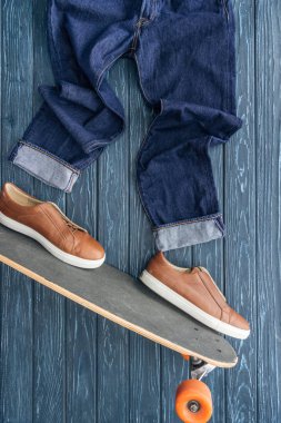 Ahşap arka plan üzerinde kot pantolon, Ayakkabı ve longboard üstten görünüm