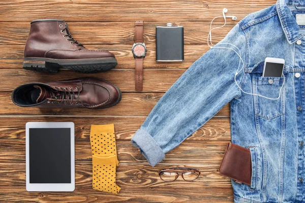 Flat lay of boots, denim jacket and digital devices on wooden background