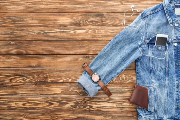 Top view of denim jacket, smartphone and accessories on wooden background