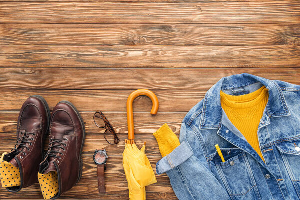 Top view of yellow umbrella, shoes and denim jacket on wooden background