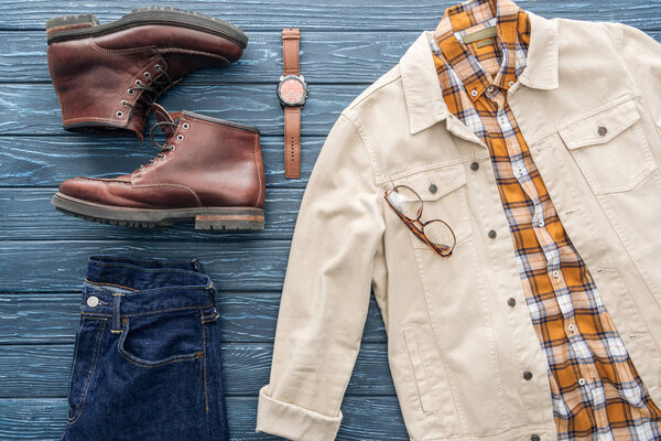 Flat lay with jeans, checkered shirt and leather boots on wooden background