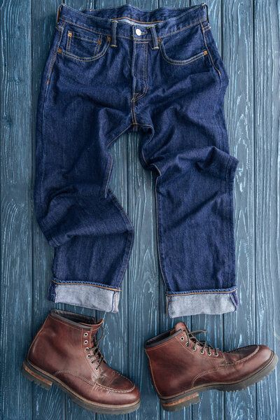 Top view of jeans and leather boots on wooden background