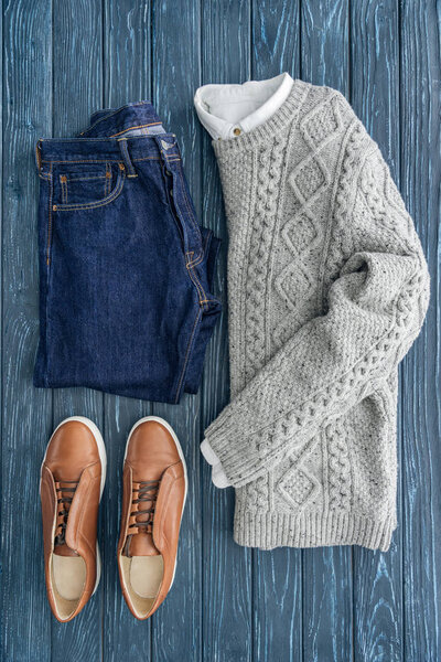 Flat lay of grey knitted sweater, jeans and shoes on wooden background