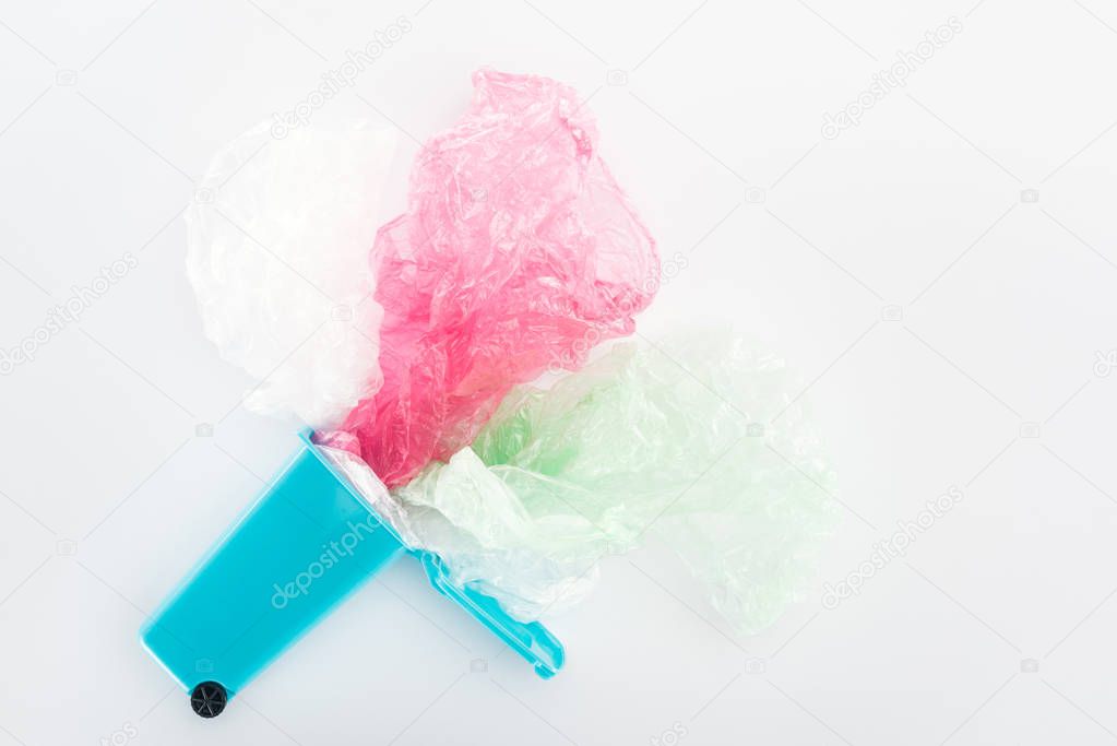 Top view of blue toy trashcan, pink and green plastic bags on grey background