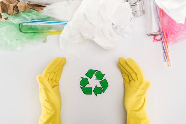Sarı lastik eldiven cam şişeler, plastik torbalar, kağıt ve geri dönüşüm sembolü ile plastik borular arasında insanın kısmi görünümü 