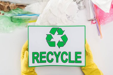 Cam şişeler, plastik torbalar, kağıt ve plastik borular arasında geri dönüşüm işareti tutarak sarı lastik eldiven insanın kısmi görünümü 