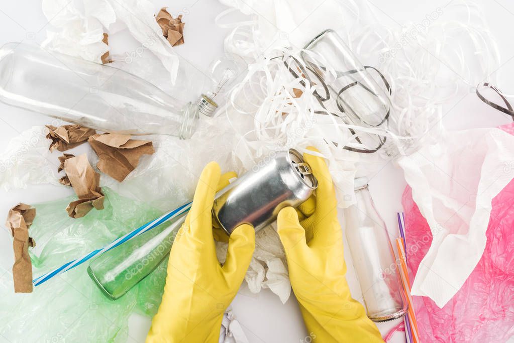 Cropped view of man holding can among glass bottles, plastic bags, paper, paper strips and plastic tubes