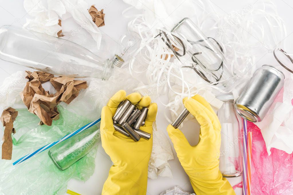 Partial view of man holding batteries among can, glass bottles, plastic bags, paper strips, paper and plastic tubes