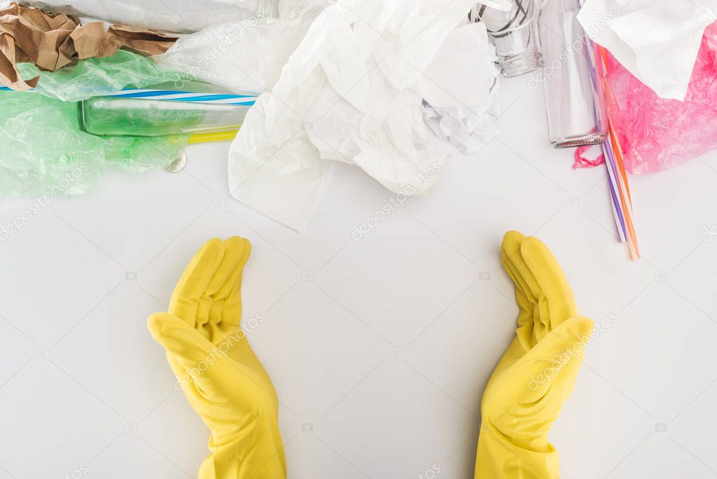 Partial view of man in yellow rubber gloves among glass bottles, plastic bags, paper and plastic tubes 
