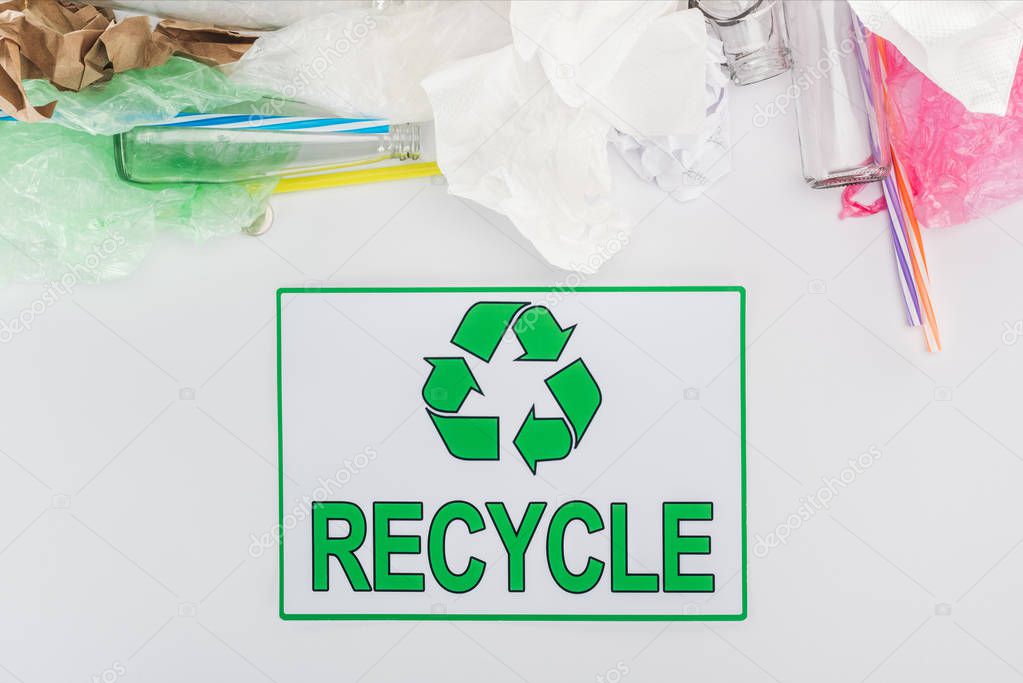 Glass bottles, plastic bags, paper and plastic tubes with recycling sign on grey background