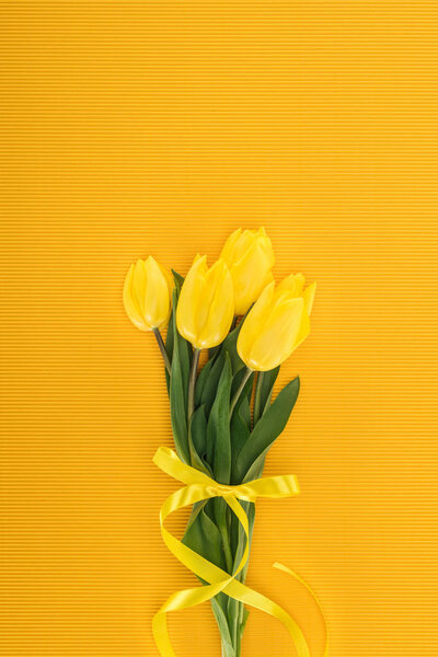 top view of yellow tulip bouquet with ribbon on orange background