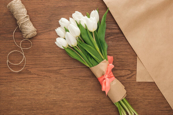 top view of spring tulip bouquet and craft paper on wooden background 