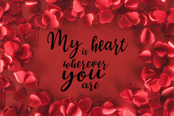 top view of decorative heart shaped petals on red background with "my heart is wherever you are" lettering, valentines day concept 