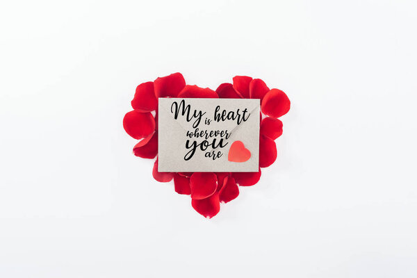 top view of envelope with "my heart is wherever you are" lettering and heart made of red rose petals isolated on white, st valentines day concept