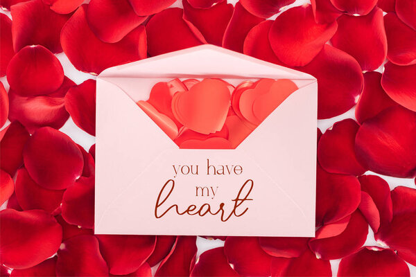 top view of envelope with "you have my heart" lettering, heart shaped confetti and red rose petals on background, st valentines day concept