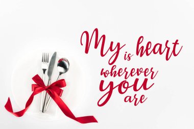 elevated view of fork, knife and spoon wrapped by red festive bow on plate isolated on white, st valentine day concept with 
