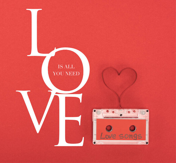 elevated view of audio cassette with lettering love songs and heart symbol made of tape isolated on red, st valentine day concept with "Love is all you need" lettering