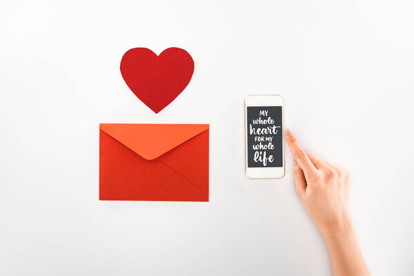 cropped image of woman holding smartphone with "my whole heart for my whole life" lettering near heart symbol and red envelope isolated on white, st valentine day concept