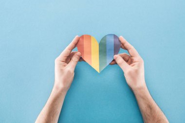 Kağıt kalp mavi arka plan, lgbt kavramı üzerinde renkli gökkuşağı ile erkek el görünümünü kırpılmış