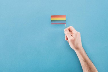 cropped view of man holding paper rainbow flag on blue background, lgbt concept clipart