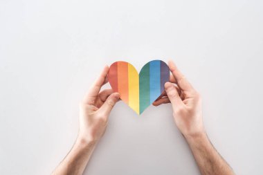 partial view of man holding rainbow colored paper heart on grey background, lgbt concept clipart