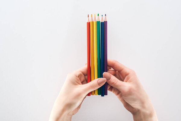 обрезанный вид женской руки с радужными карандашами на сером фоне, концепция lgbt
