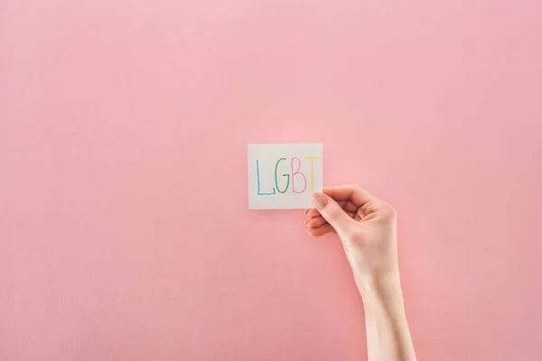 女性手的部份看法与 Lgbt 手写的简称在白色卡片在粉红色背景 — 图库照片