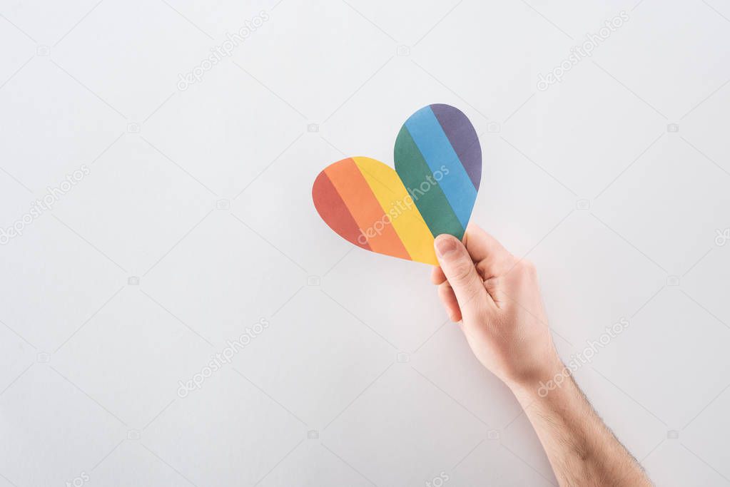 cropped view of male hand with rainbow colored paper heart on grey background, lgbt concept
