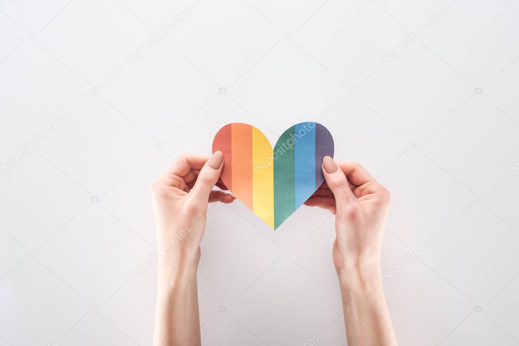 partial view of woman holding rainbow colored paper heart on grey background, lgbt concept