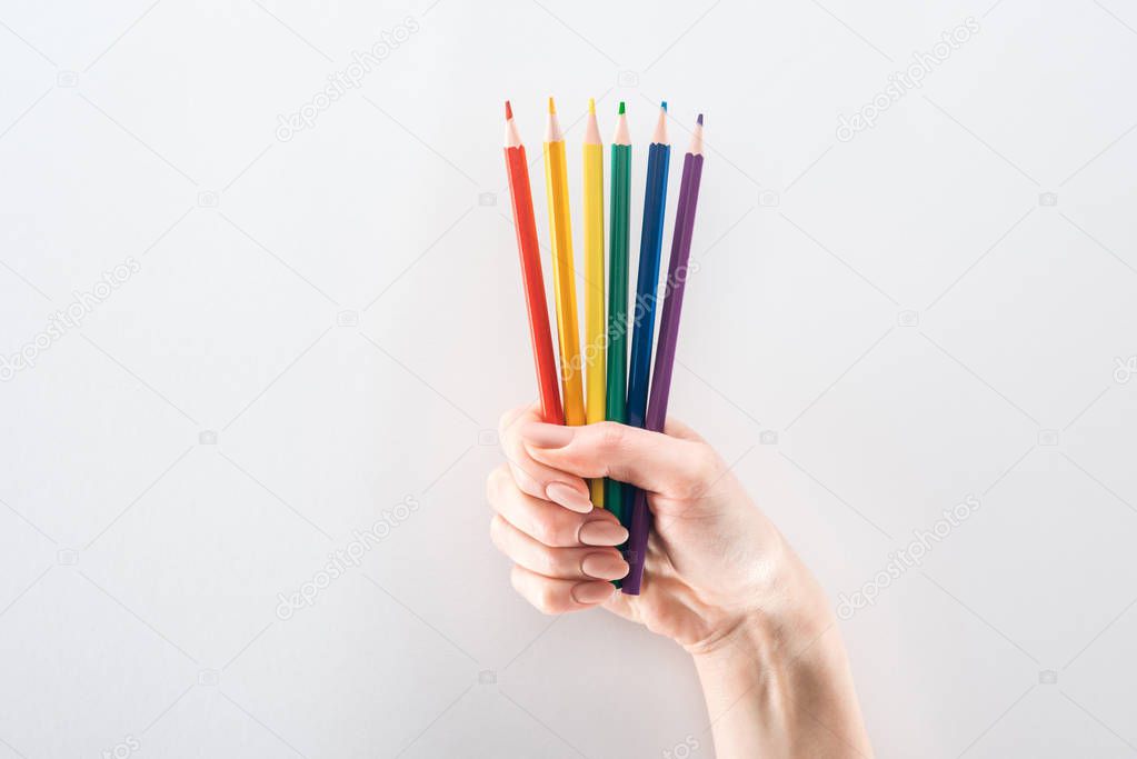 partial view of female hand with rainbow colored pencils isolated on grey, lgbt concept