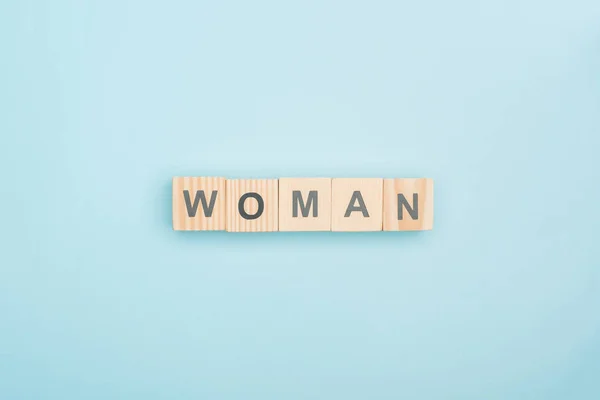 蓝色背景上由木制立方体制成的妇女字母的顶部视图 — 图库照片