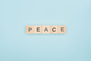 top view of peace lettering made of wooden cubes on blue background clipart