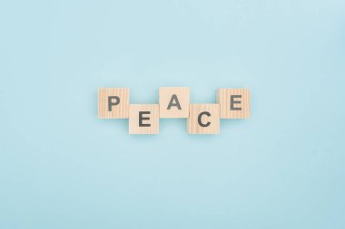 top view of peace lettering made of wooden blocks on blue background clipart