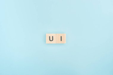 top view of ui lettering made of wooden cubes on blue background clipart