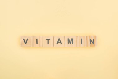 top view of vitamin lettering made of wooden cubes on yellow background clipart
