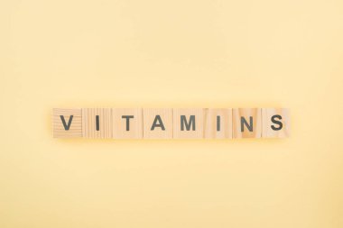 top view of vitamins lettering made of wooden cubes on yellow background clipart