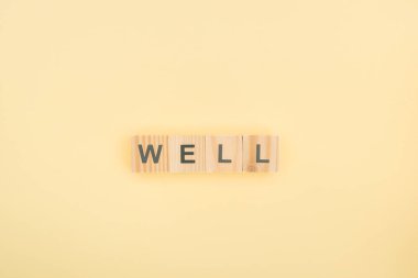 top view of well lettering made of wooden cubes on yellow background clipart