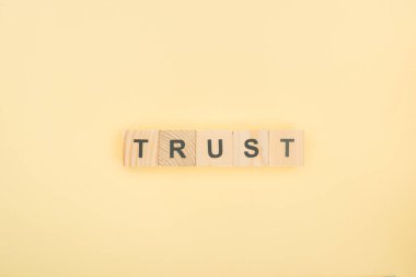 top view of trust lettering made of wooden cubes on yellow background clipart