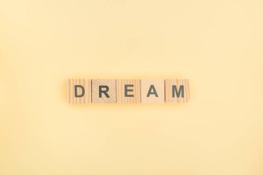 top view of dream lettering made of wooden cubes on yellow background clipart